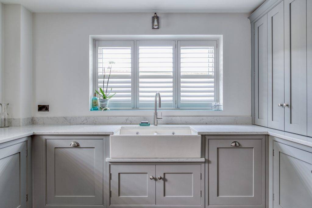 Gray kitchen cupboards with a belfast sink window centerd above the sink with white wooden blinds 