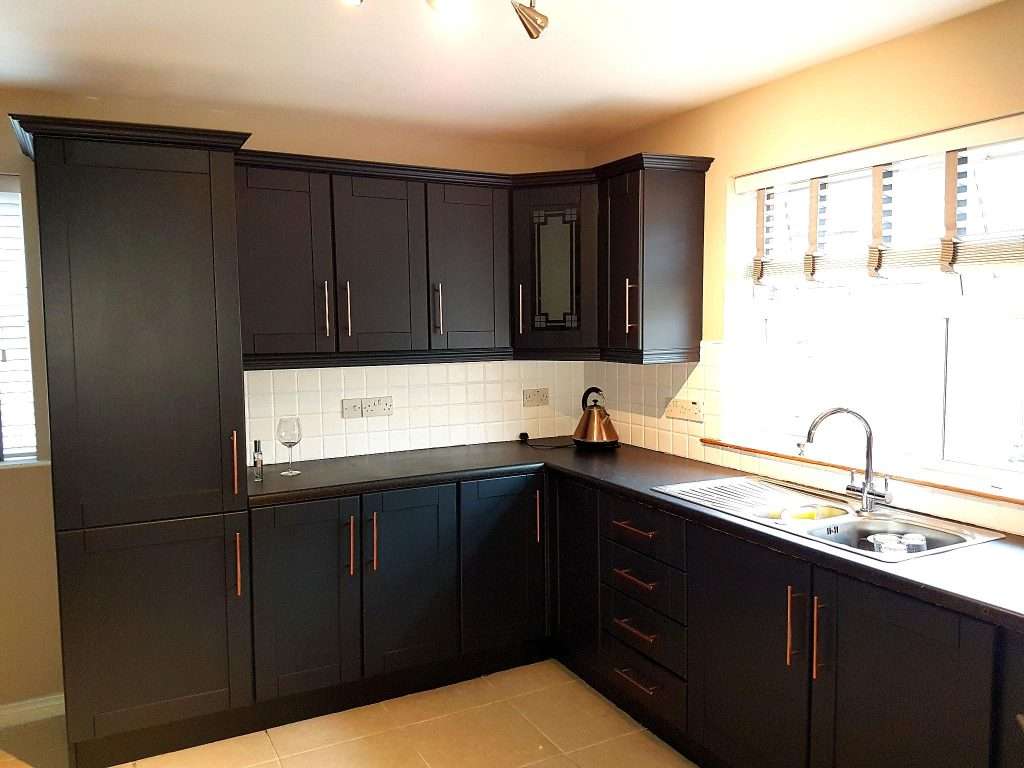 Sleek black Cabinetry in a modern kitchen with ample storage space, a window with blinds for natural light, and a stainless steel sink, showcasing professional interior painting by G&E Interior Painting in Portstewart.