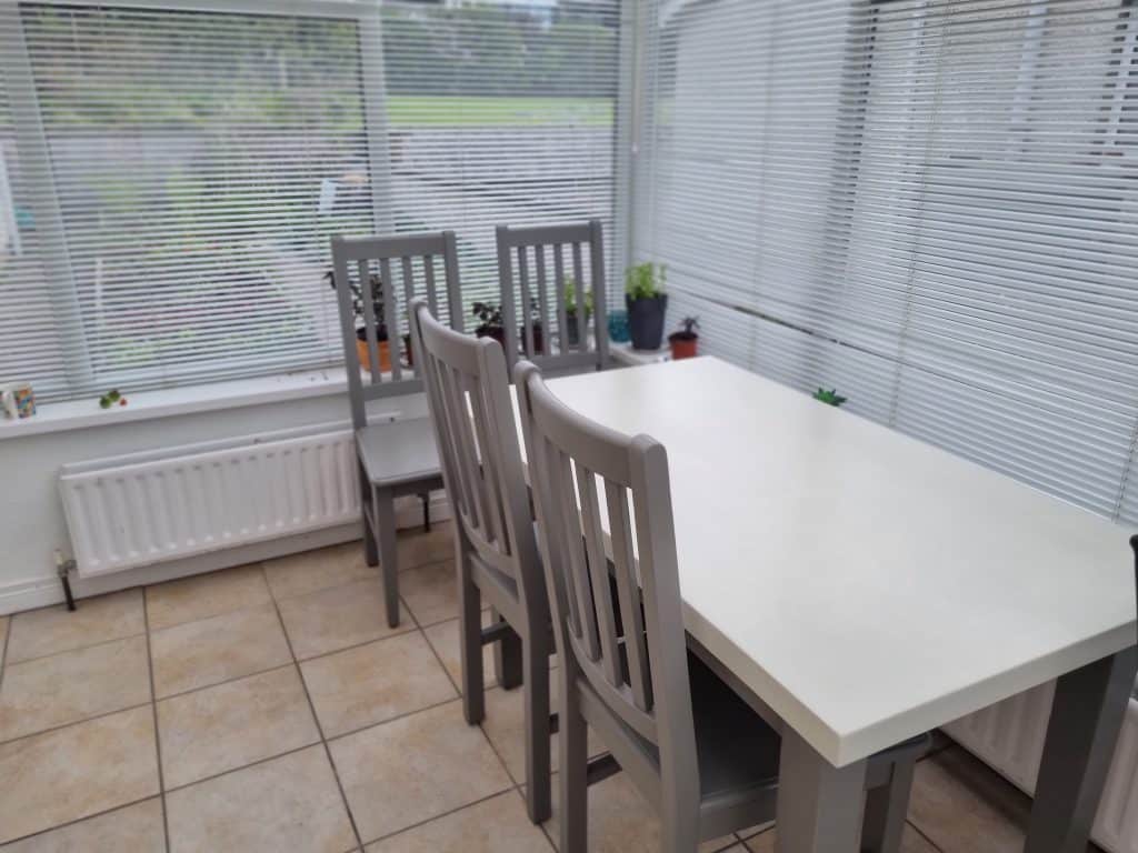 Bright interior dining area with white table, gray chairs, and large windows with white blinds, showcasing professional interior painting services in Portstewart.