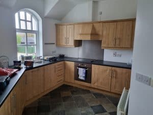 Culinary kitchen with natural wooden cabinets, black countertops, kitchen appliances, and large arched window in Portstewart, showcasing expert interior painting services.